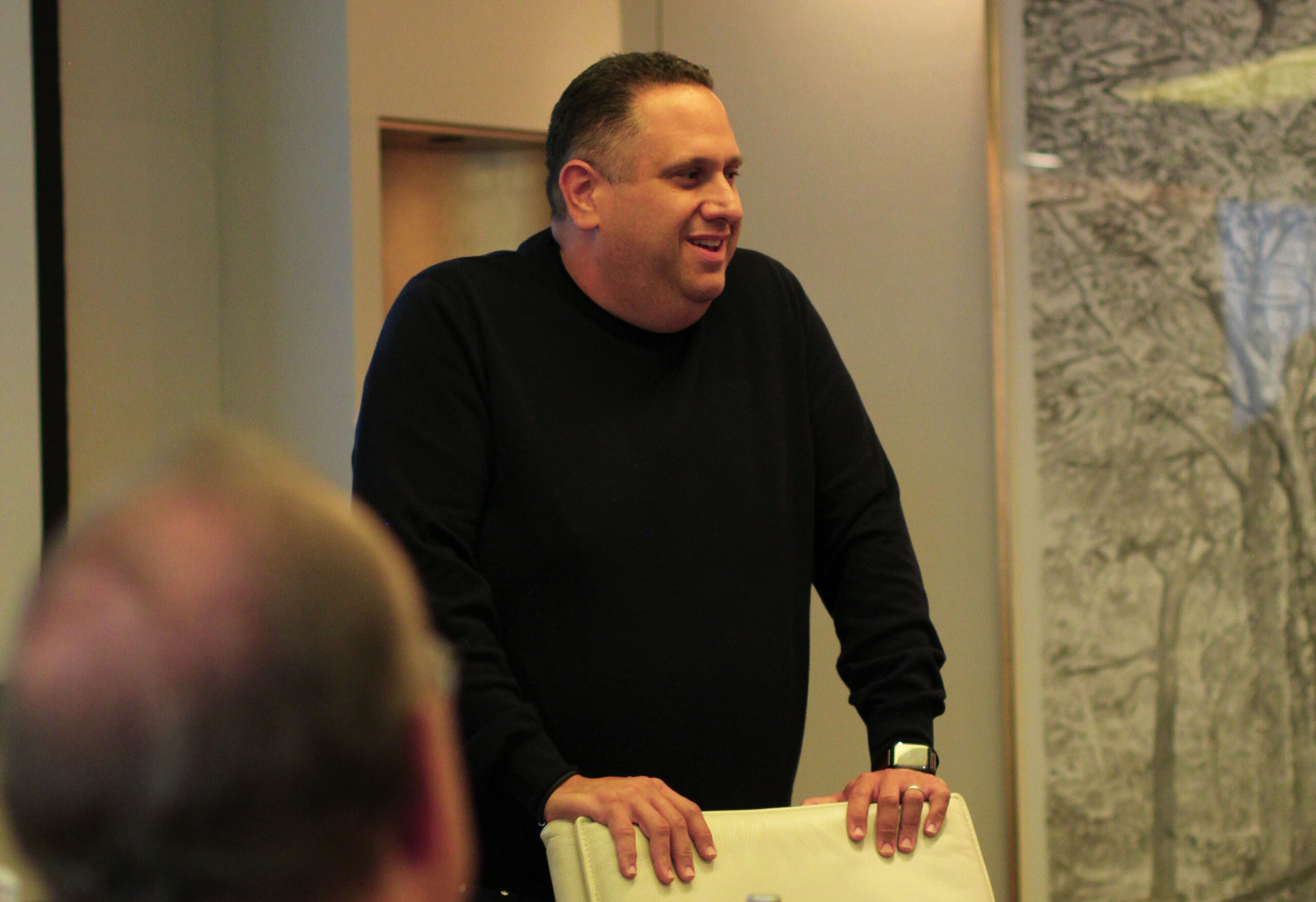 Man standing in conference room with hands on a whit chair